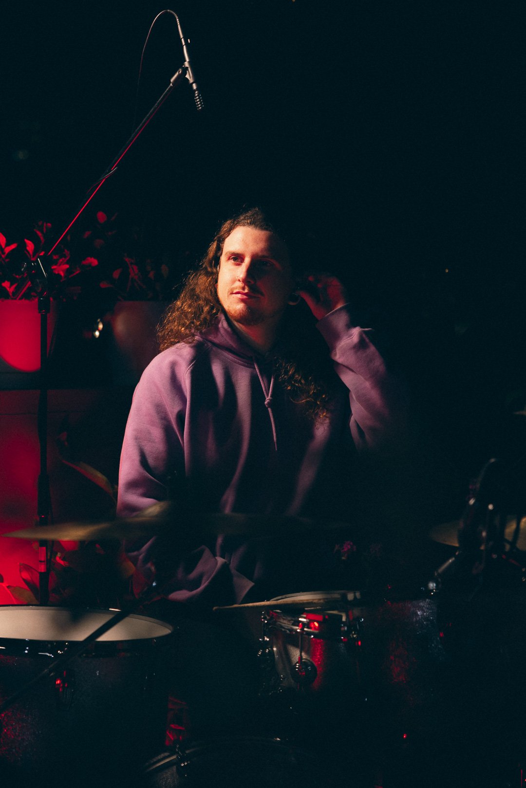 Drummer seated at kit under red lights during rooftop performance.