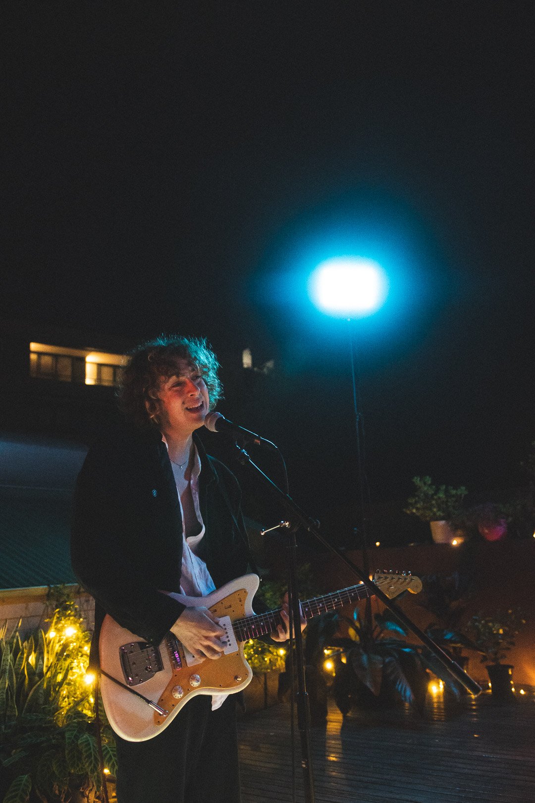 Olive Rush of EGOISM singing into microphone while playing guitar on rooftop.