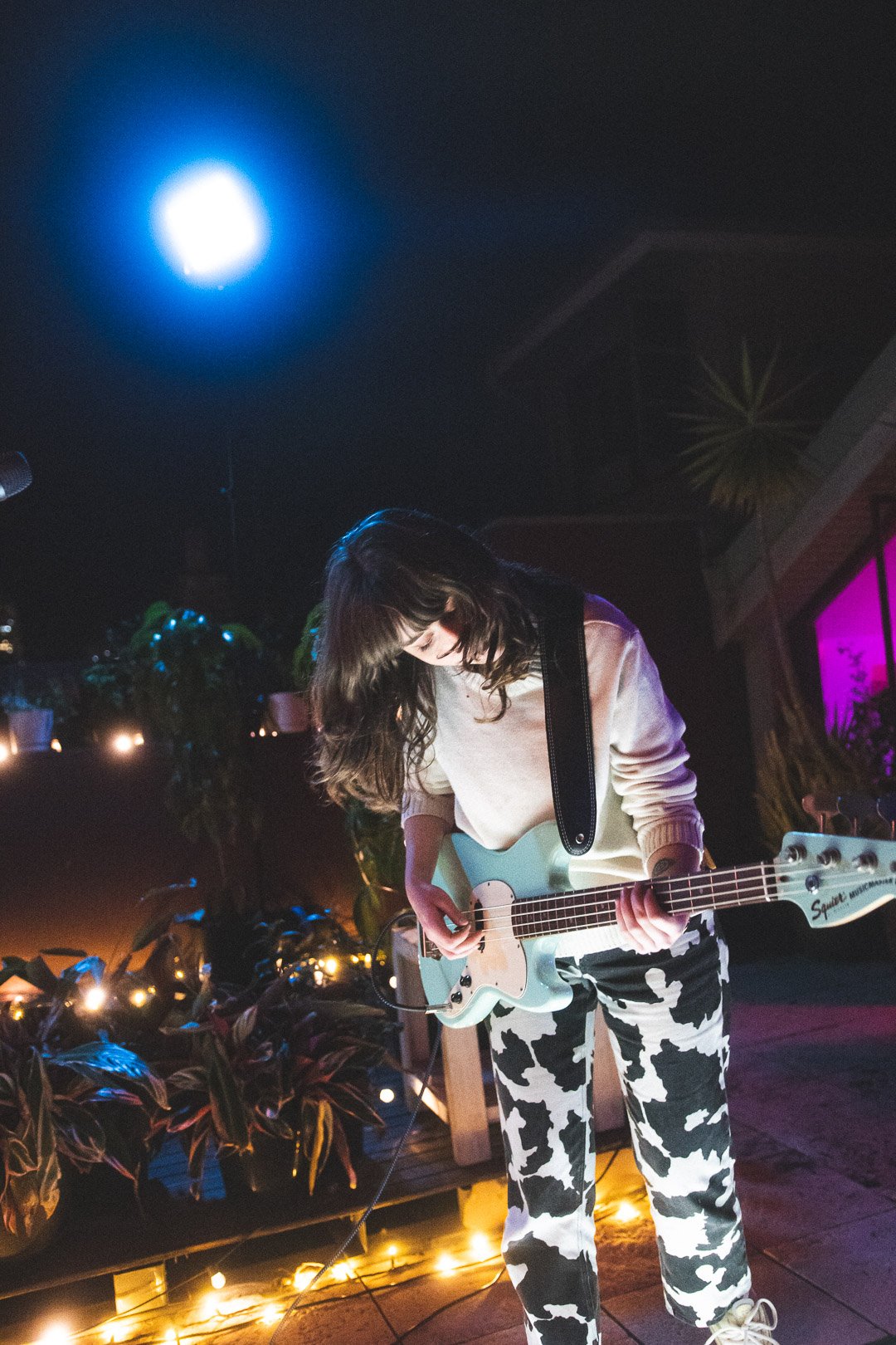 Scout Eastment of EGOISM leaning forward while playing bass guitar on the rooftop stage.