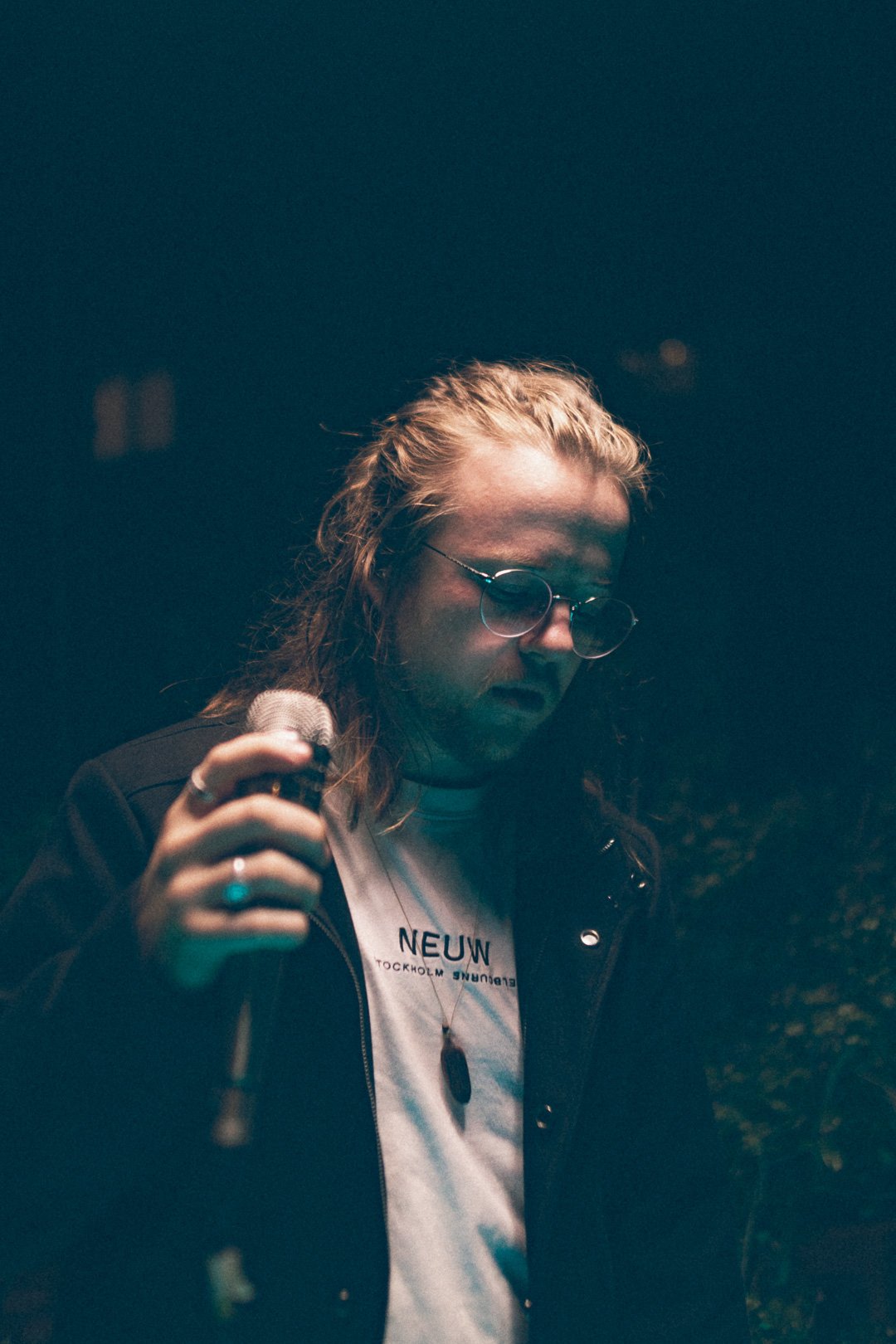 Ben Woolner of SAFIA holding microphone under moody blue rooftop lighting.