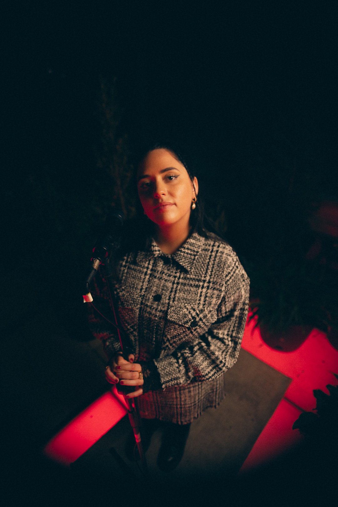 Tia Gostelow standing at microphone under red lighting on the rooftop stage.