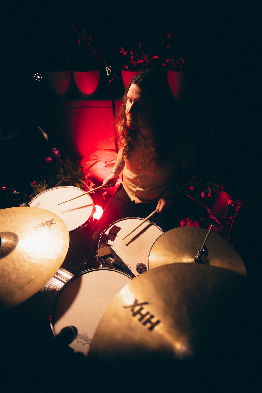 Overhead view of drummer playing kit beneath warm stage lighting.