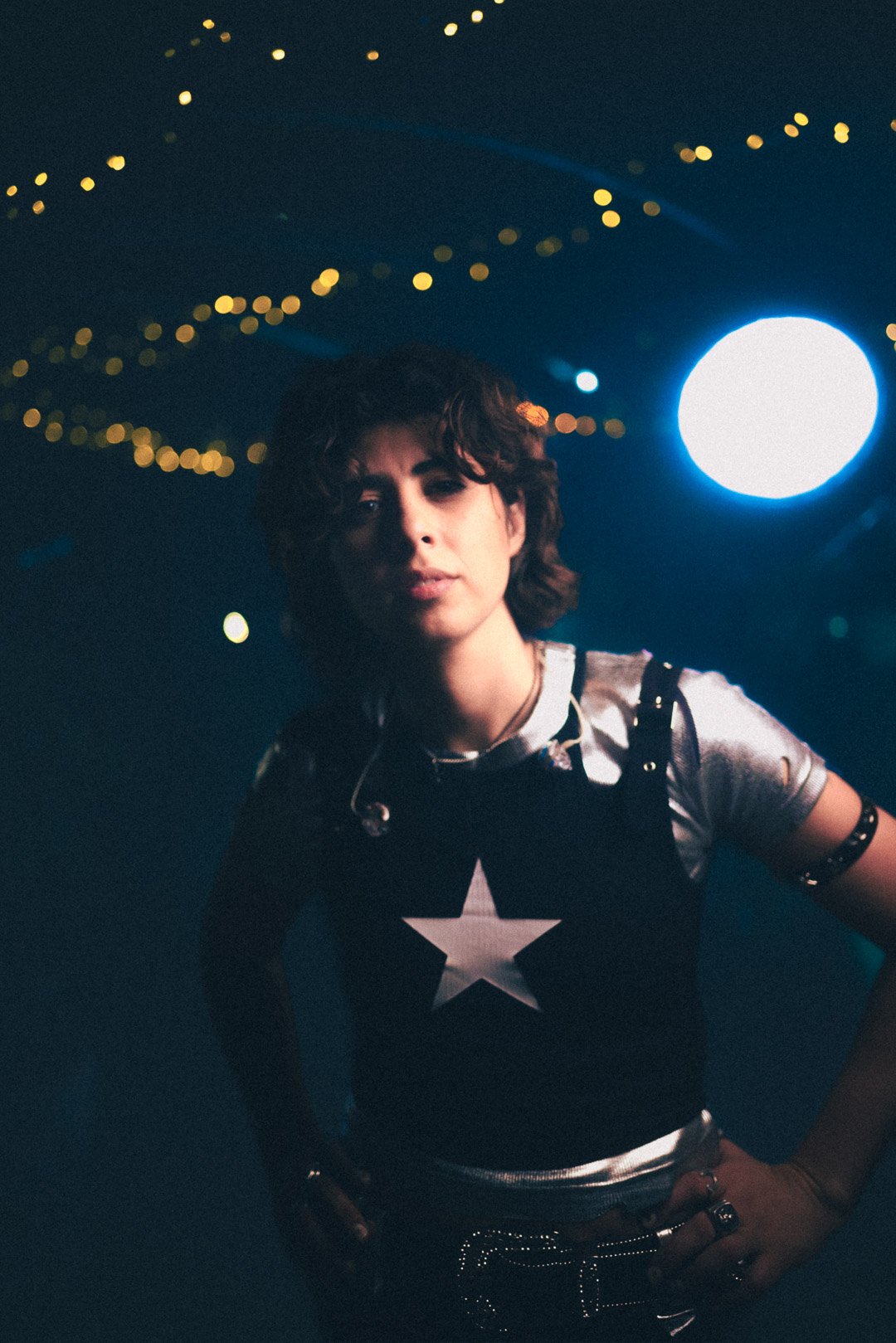 Carla Wehbe holding microphone, standing calmly under red rooftop lighting.