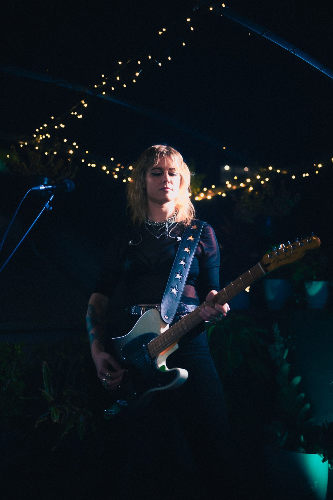 Guitarist tilting head while strumming guitar under soft evening lights.