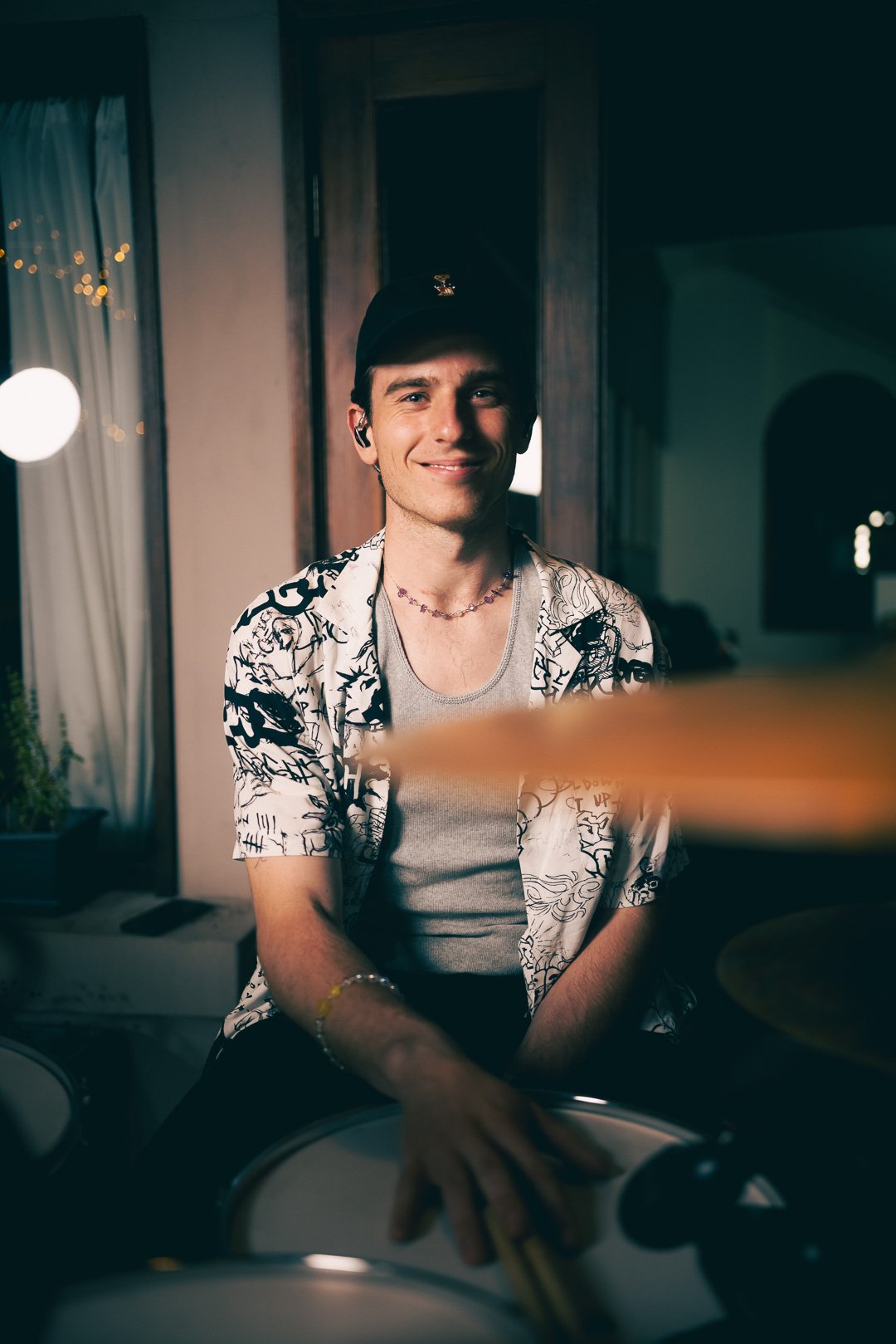 Drummer plays seated, lifting sticks between hits, smiling mid-performance.