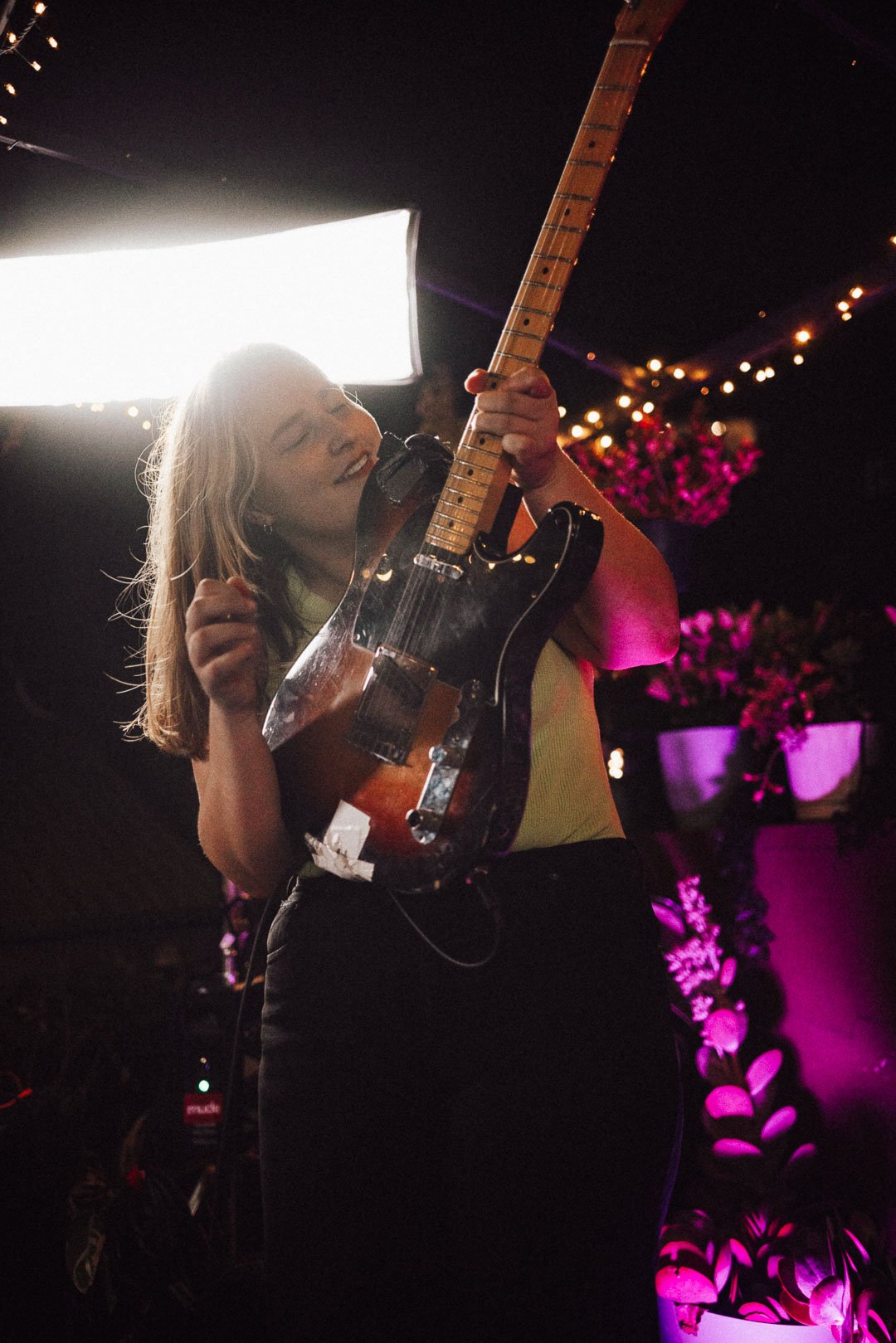 A guitarist from The Buoys leans back mid-performance, smiling as she plays an electric guitar.
