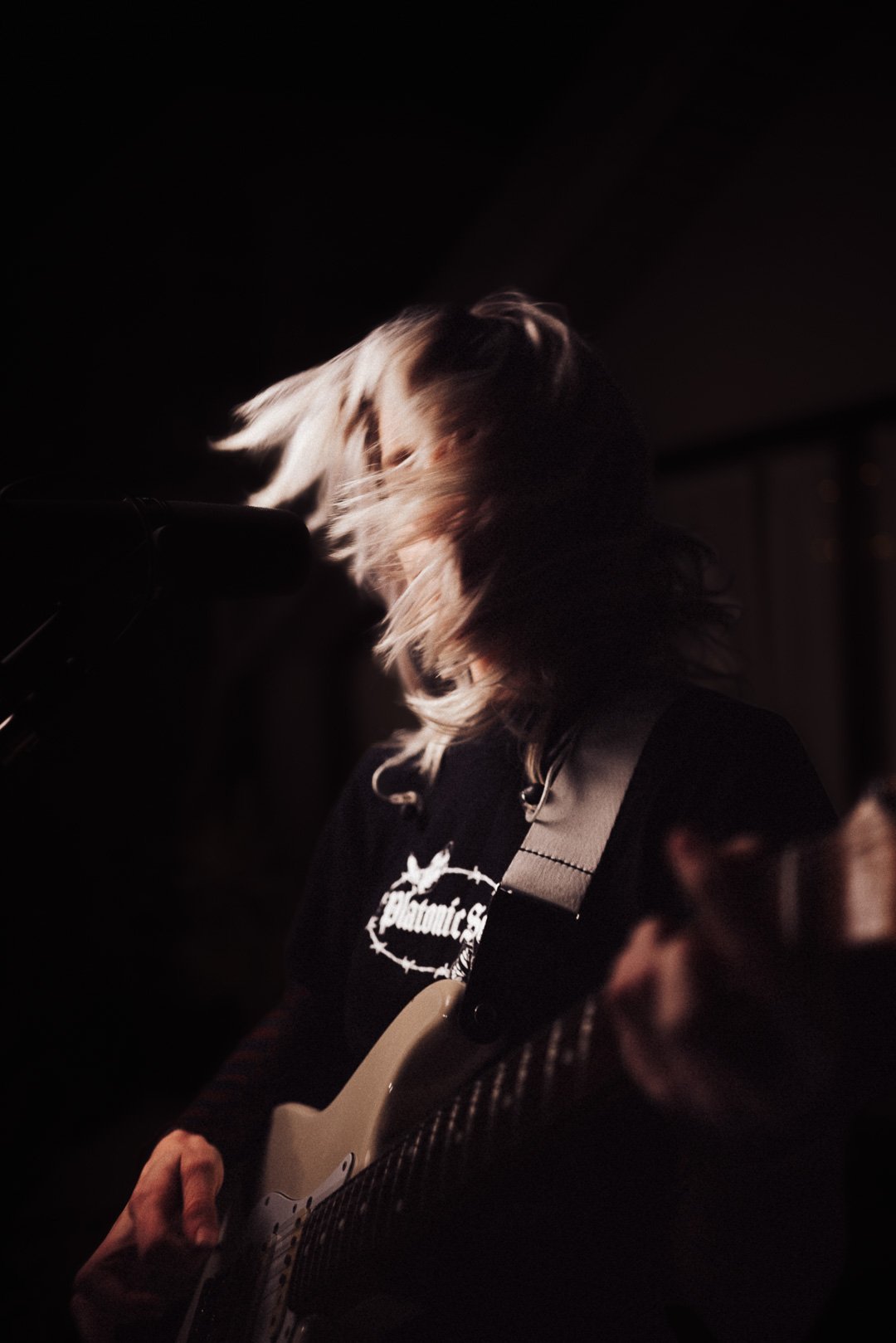 Zoe Catterall of The Buoys playing rhythm guitar with hair in motion under stage lighting