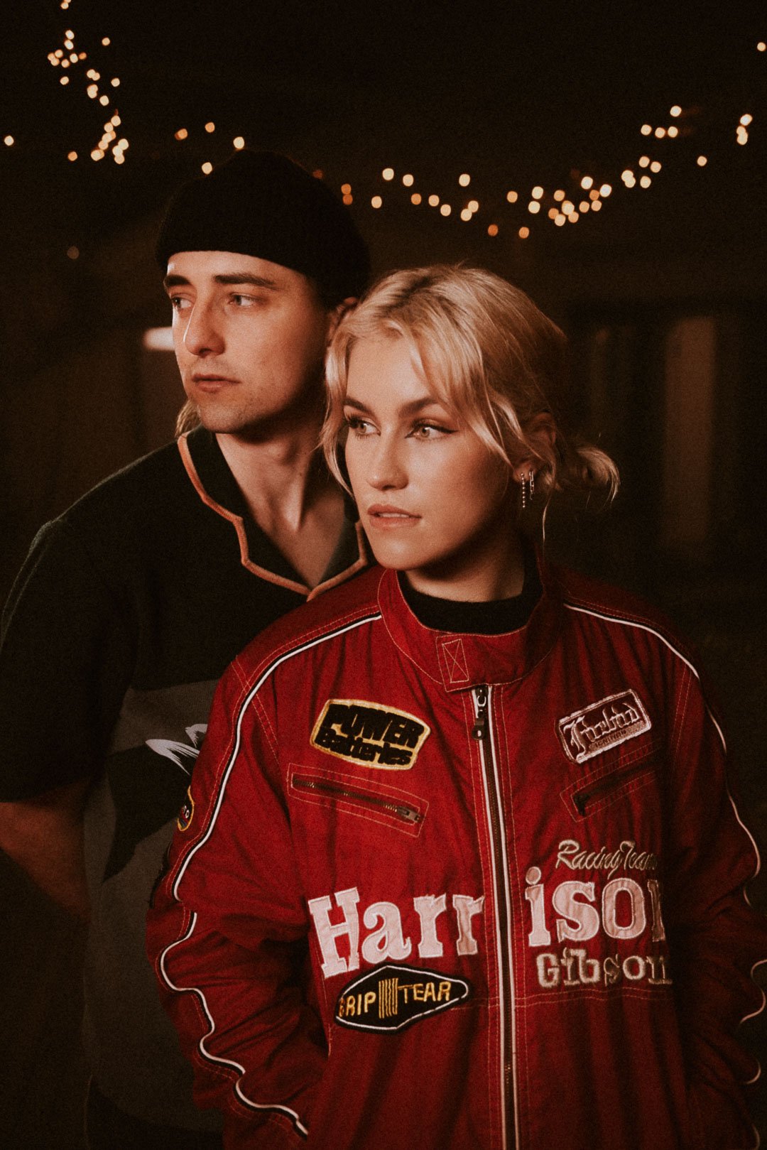 Foley standing side by side under warm string lights, looking off stage before their set.