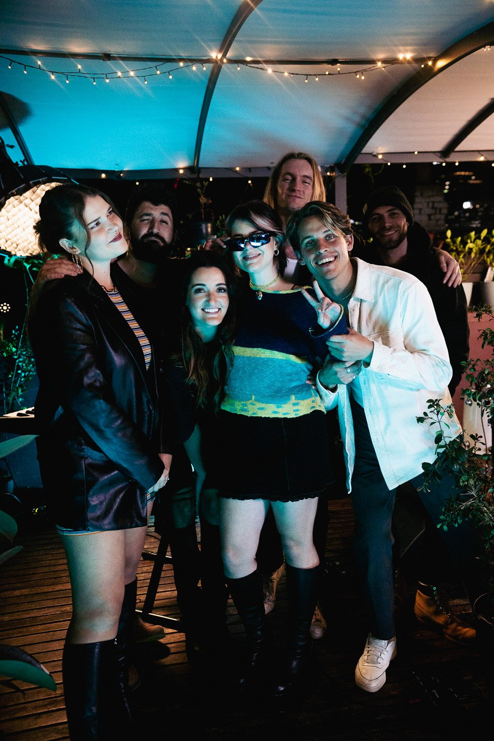 Lola Scott posing with band and crew under string lights on rooftop.
