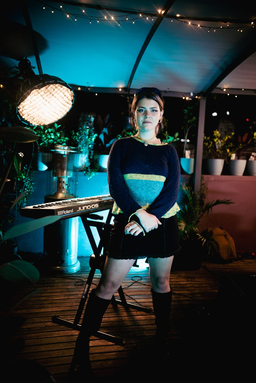 Lola Scott standing beside keyboard under studio lights on rooftop set.