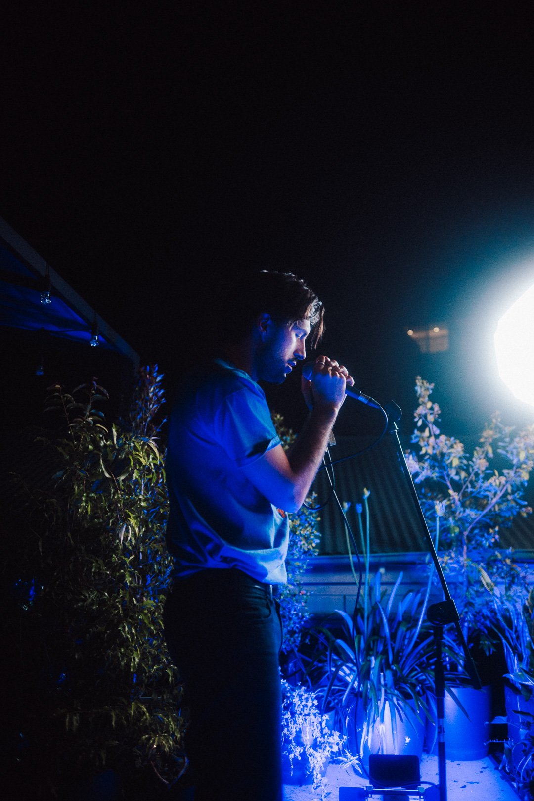 Charlie Kerr of Hotel Mira singing into microphone under cool blue rooftop lighting