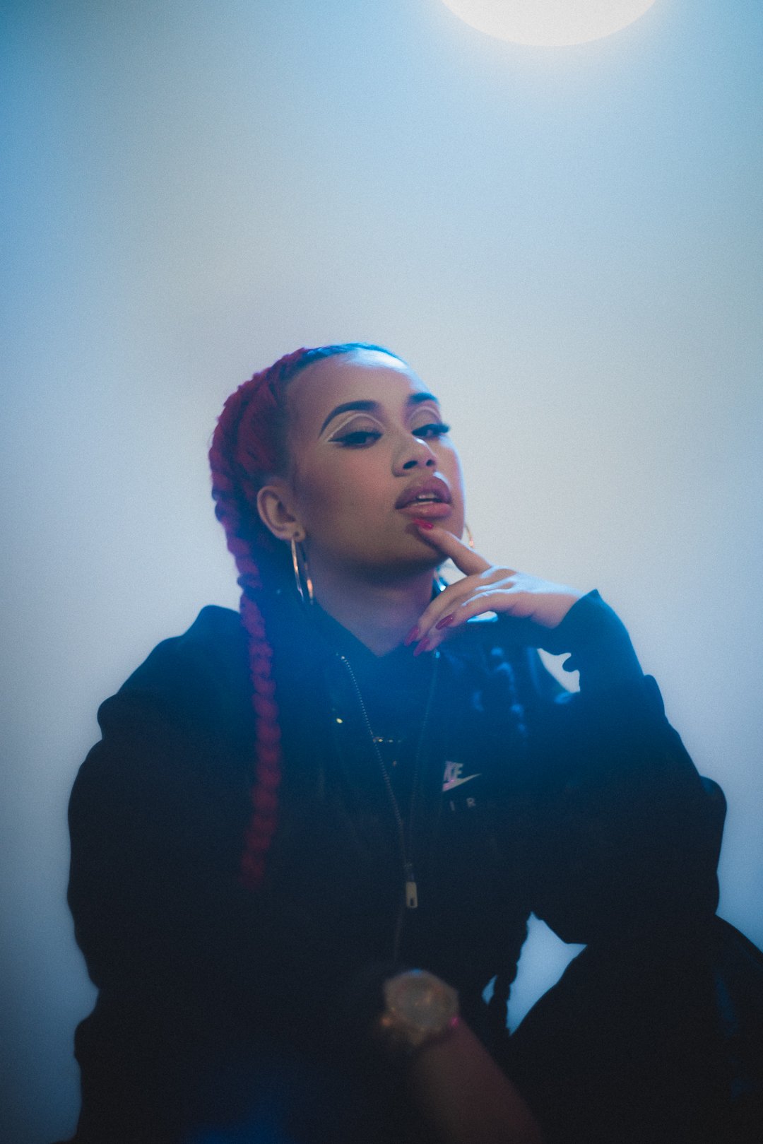 .GIRL close-up portrait with braids and hoop earrings under cool blue lighting.