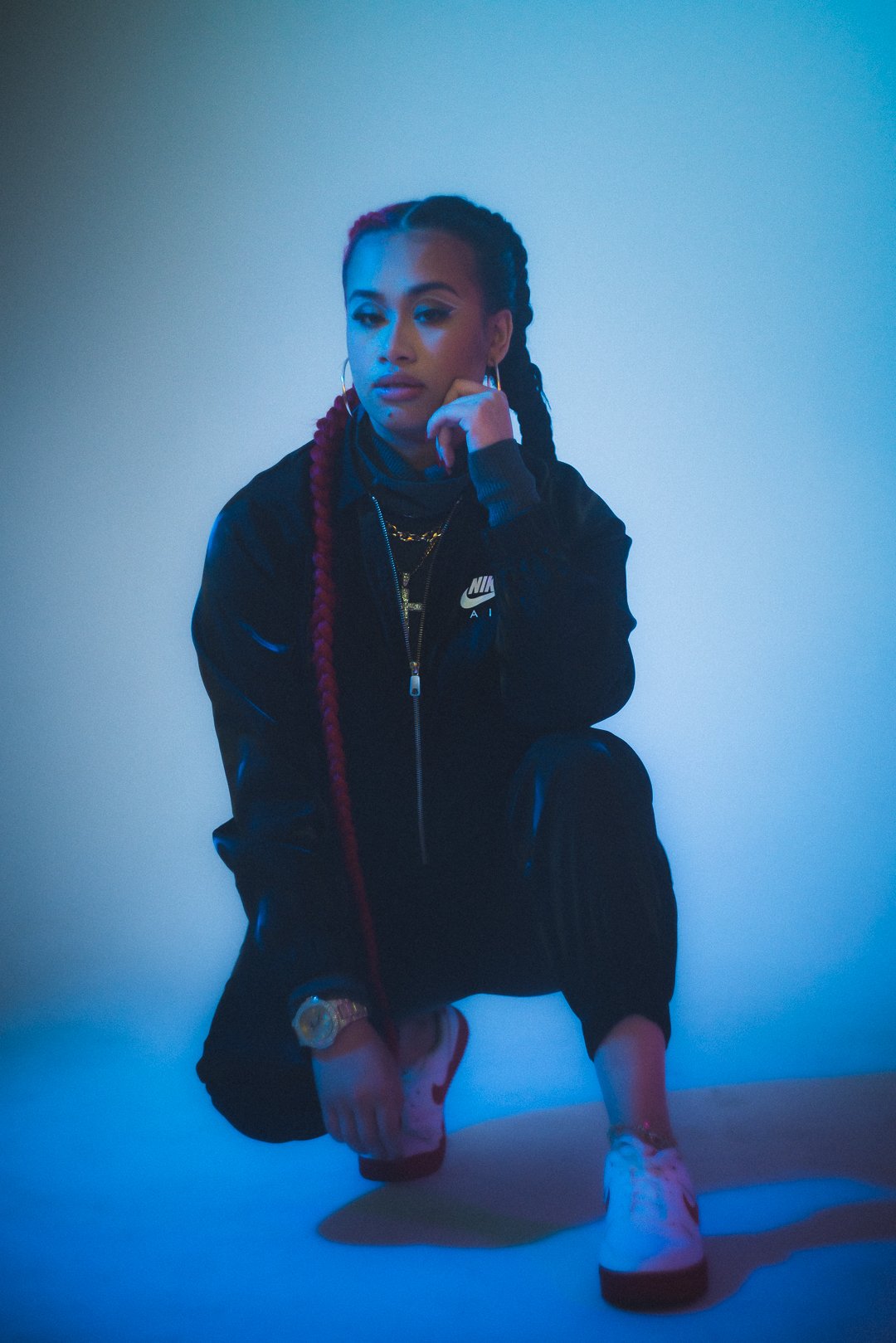 A.GIRL crouching in studio wearing dark tracksuit under cool gradient lighting