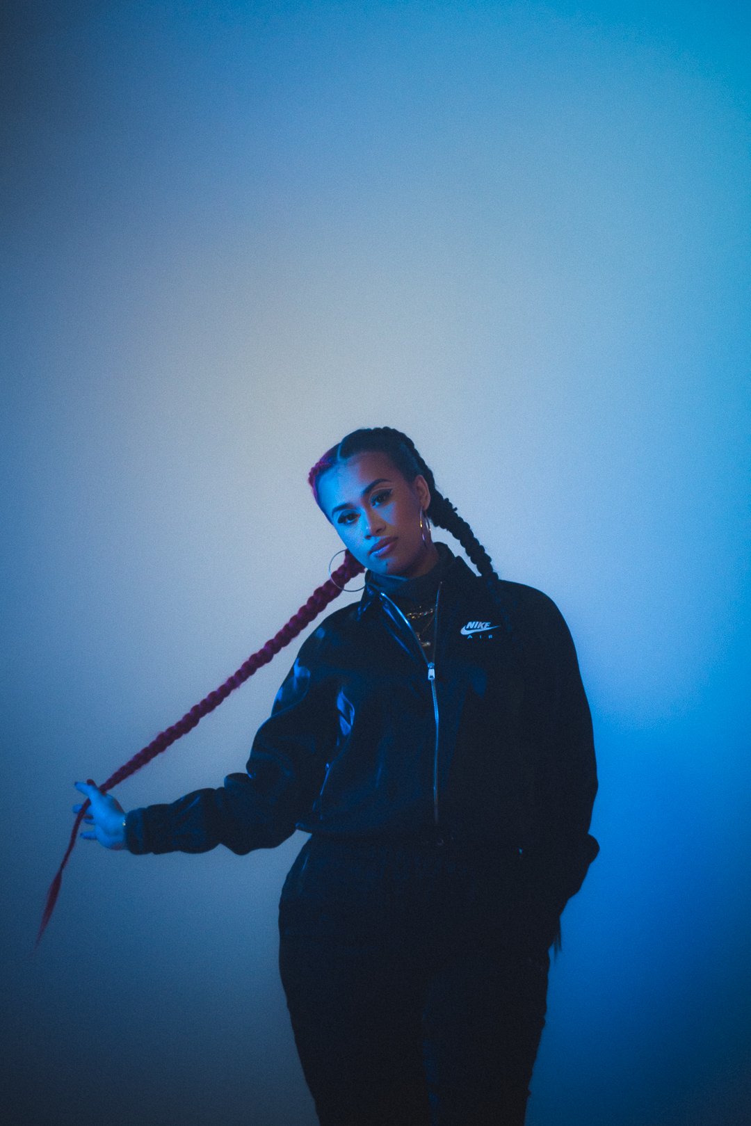 A.GIRL standing in studio holding braided hair under cool blue lighting