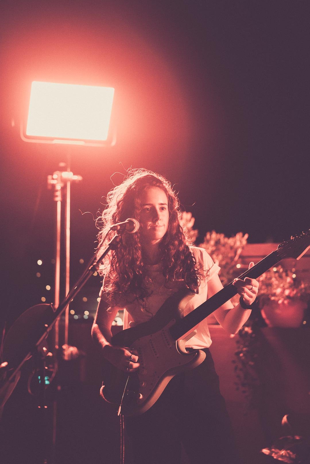 live band holding electric guitar beneath rooftop lighting during live performance