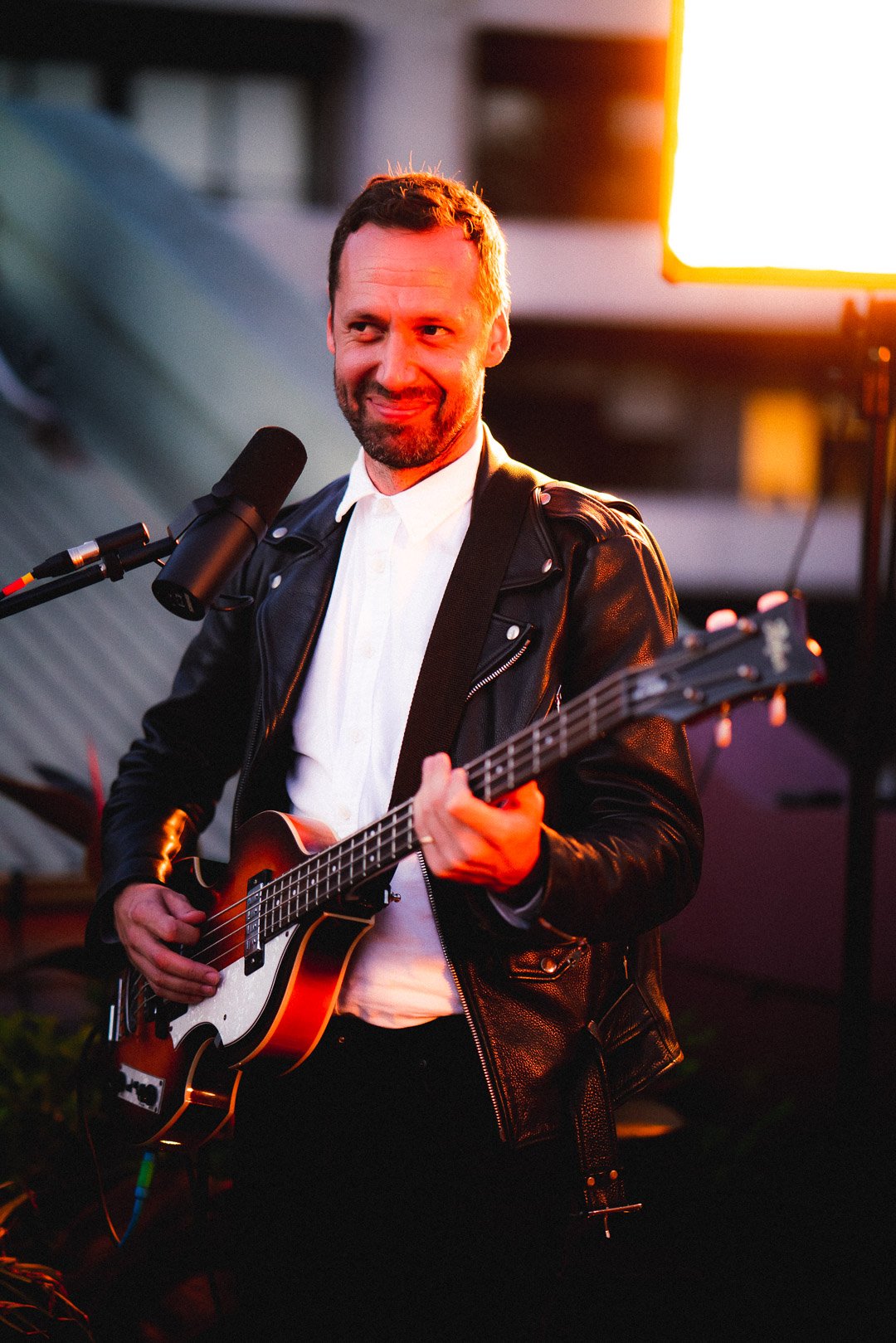 Joshua Moriarty of Telenova playing bass guitar on rooftop stage under warm lights.