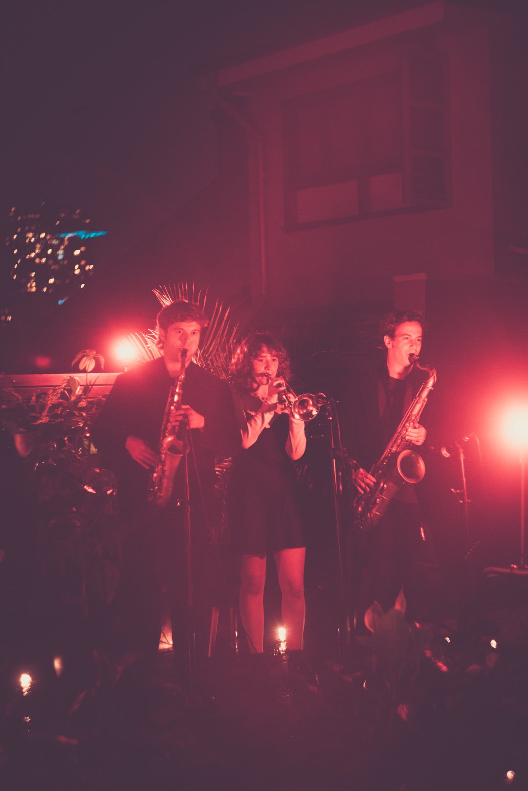 Horn section performing together under warm red lighting during the rooftop live set