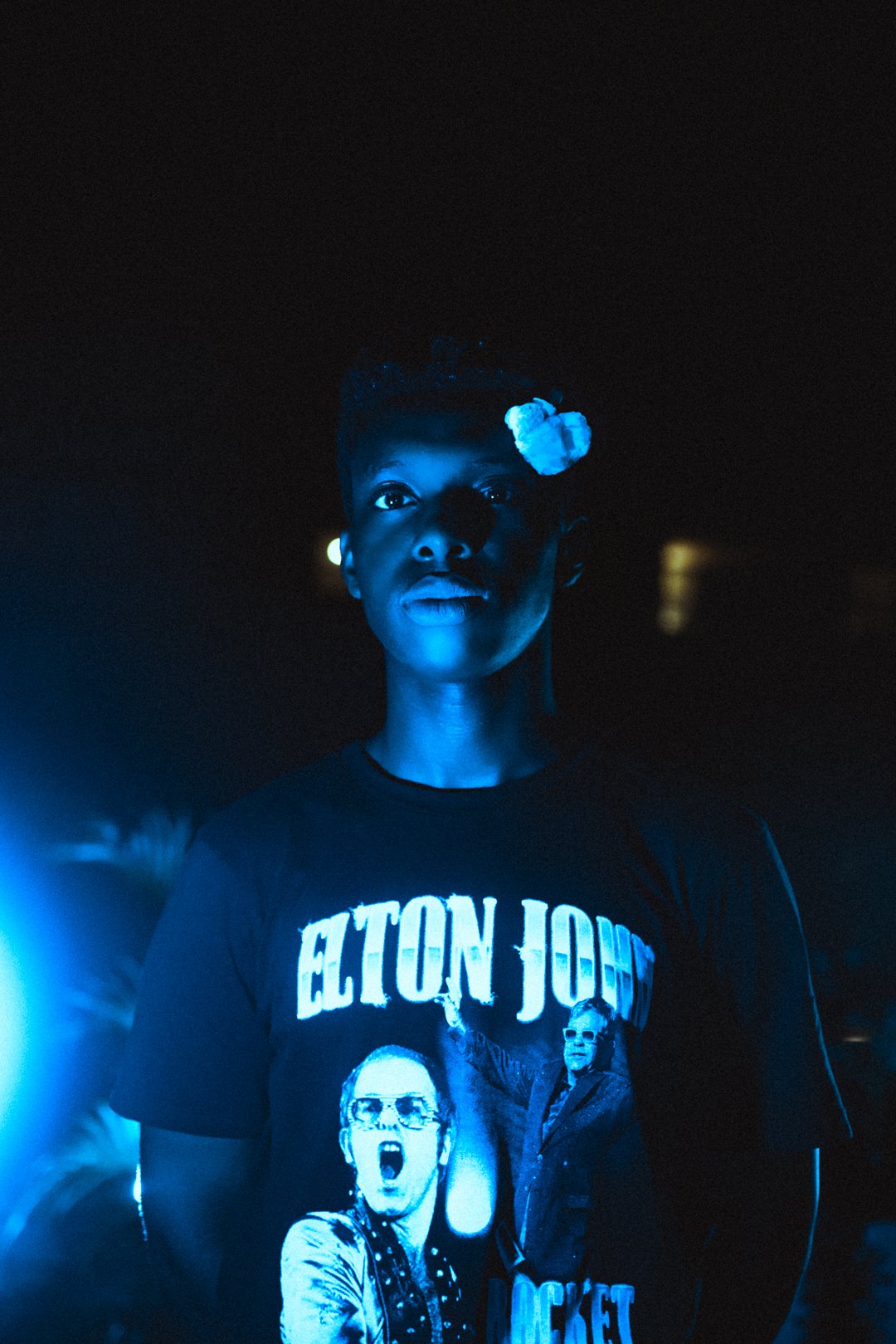 Stevan facing camera under blue light with small flower tucked in hair.