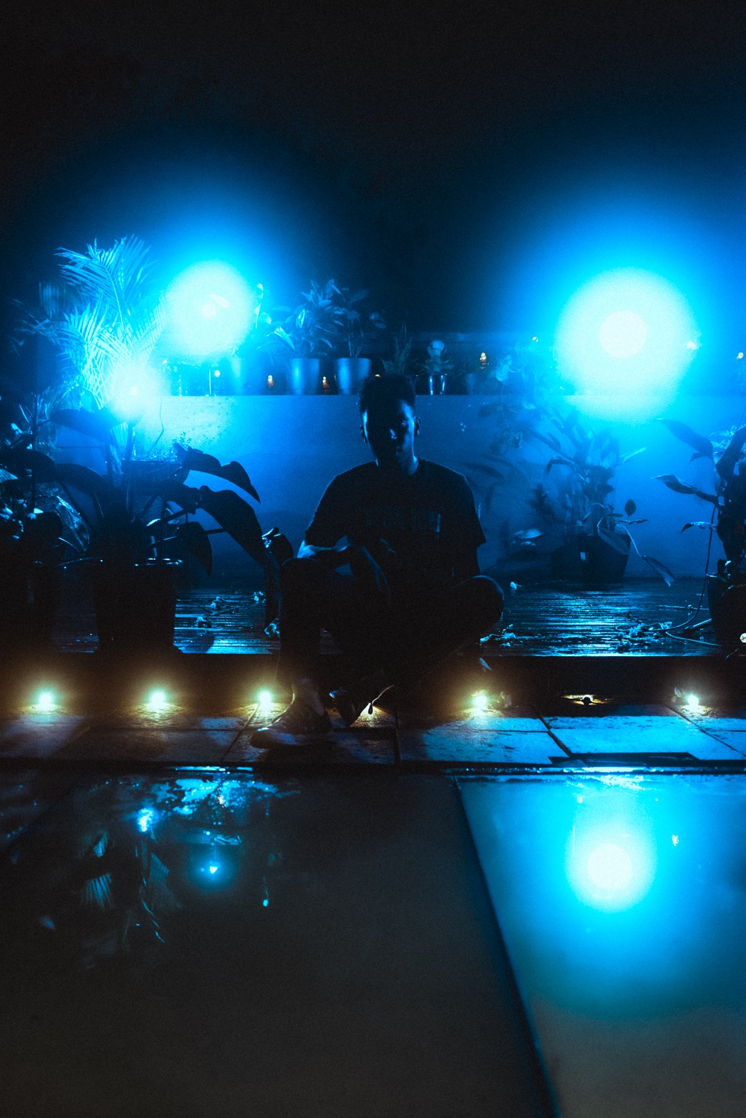 Wide rooftop shot of Stevan seated under bright blue lights at night.