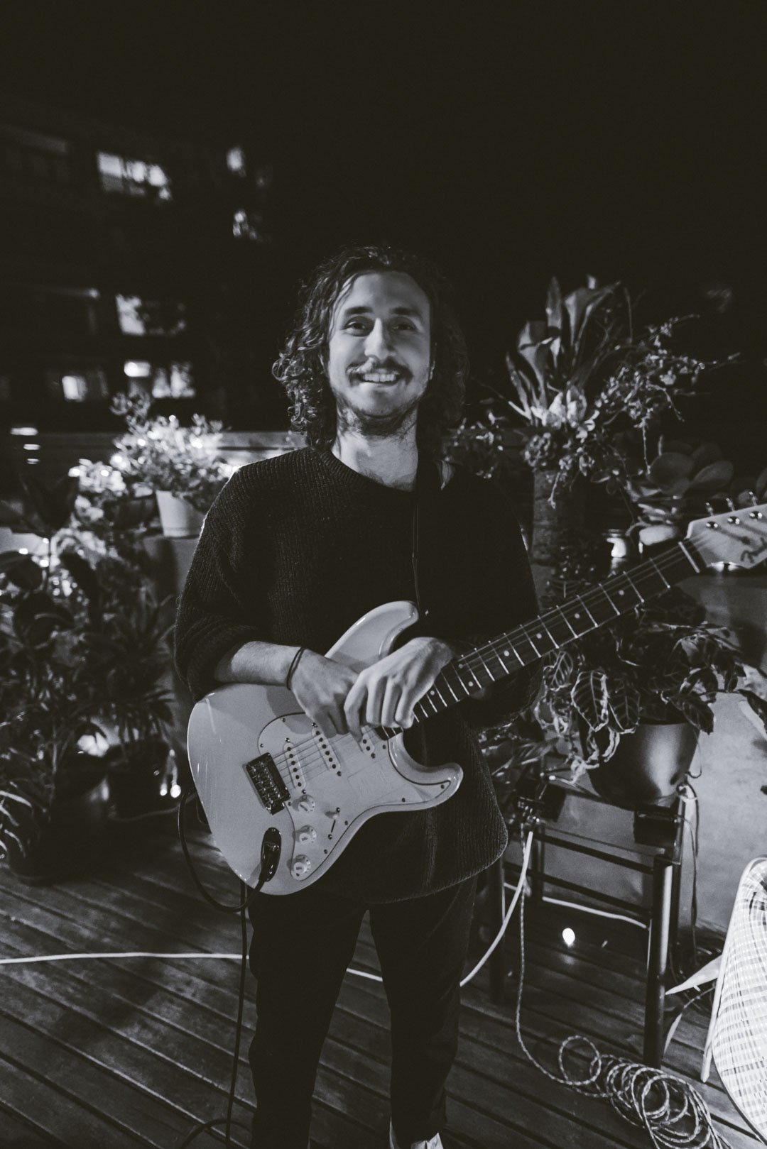 Black and white portrait of the live guitarist holding an electric guitar on the roof.