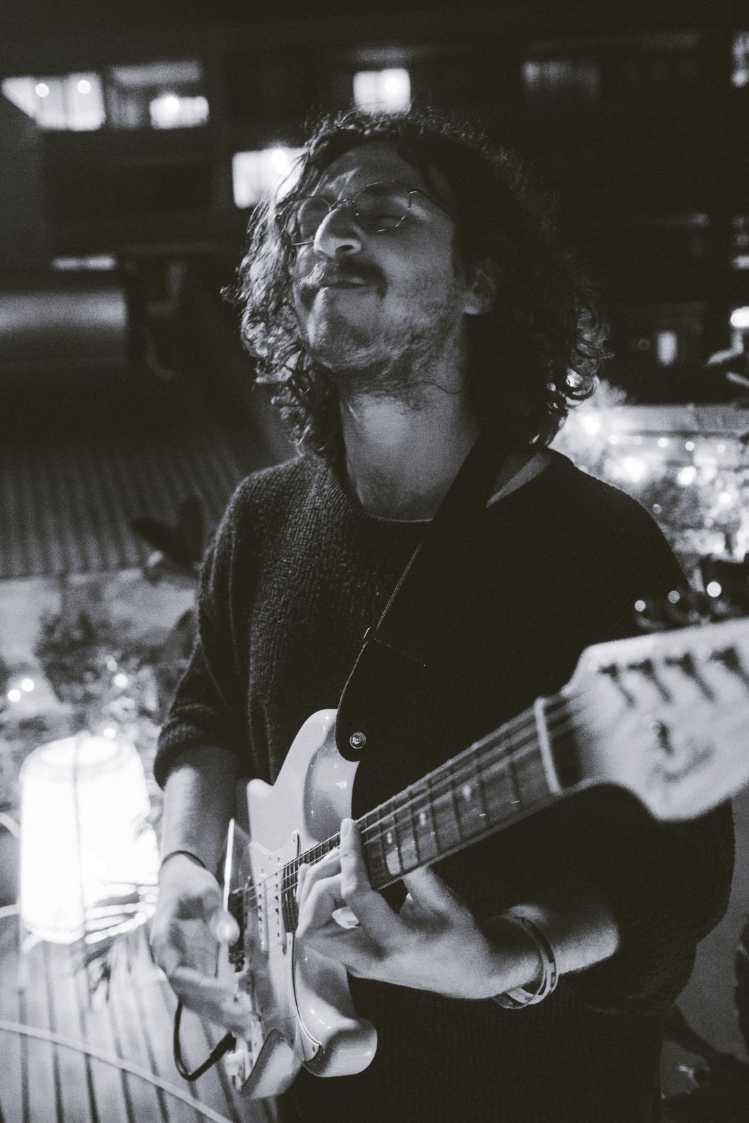 Guitarist smiling mid-performance with city lights blurred in the background.