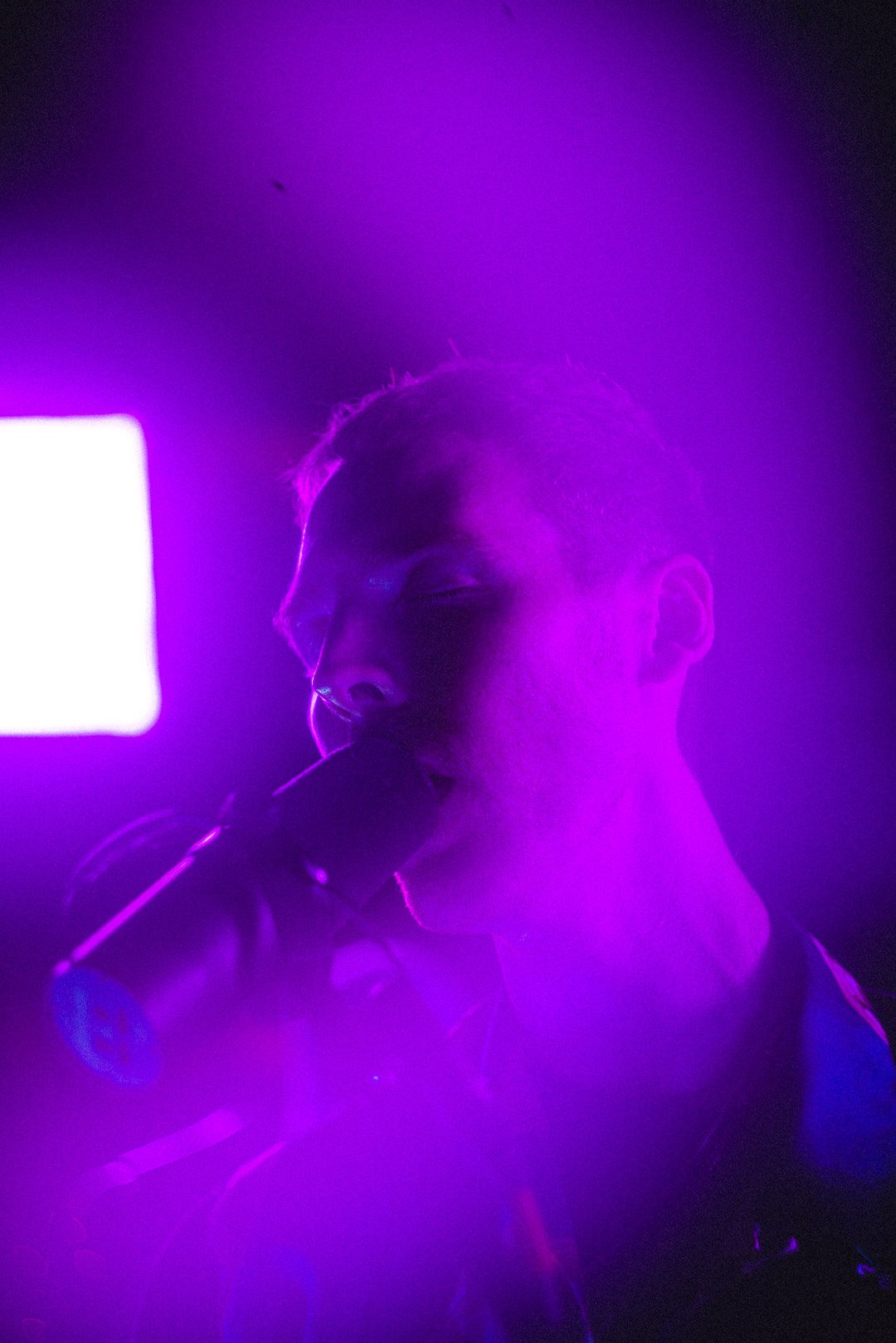 Close-up of Skeleten singing into microphone surrounded by purple stage light.