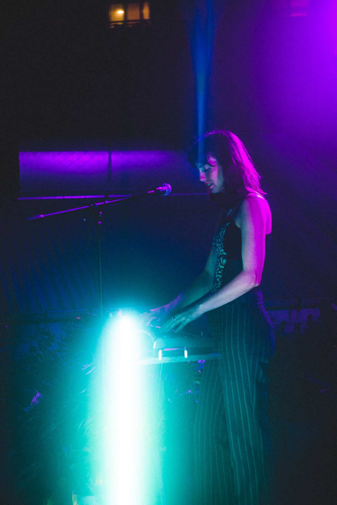 Keyboard performance captured from the side, glowing teal and purple stage lights.
