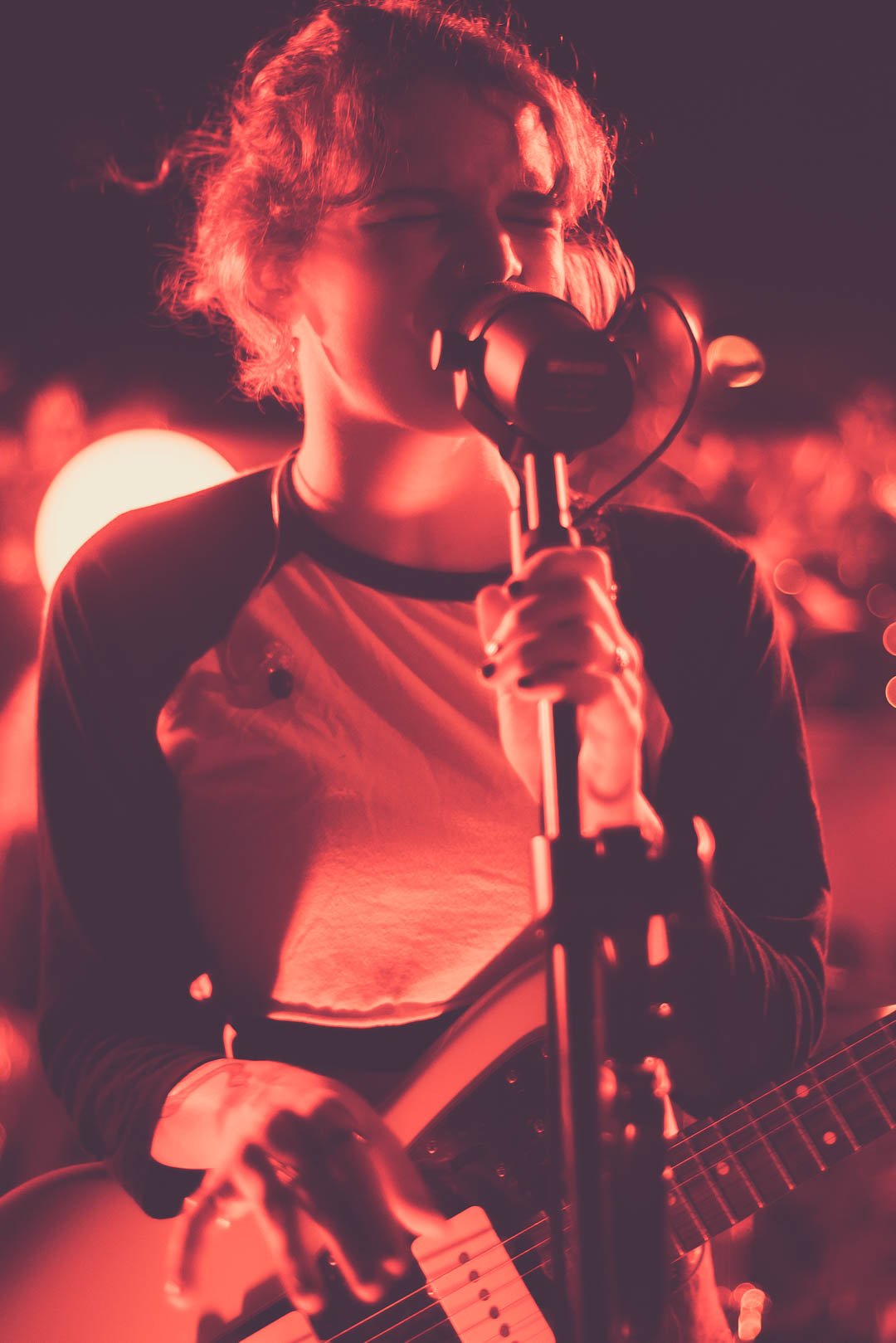 Close-up of MAY-A singing into microphone with guitar.